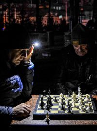 Muži v kyjevském parku hrají šachy, svítit si musí baterkou. Kvůli ruskému jsou v celé zemi výpadky elektrického proudu.