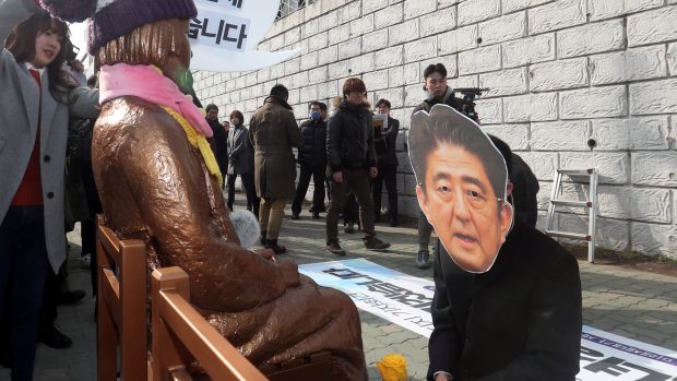 Aktivista s maskou japonského premiéra Abeho klečí u sochy sexuální otrokyně před japonským konzulátem v Pusanu.