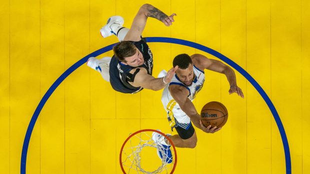 Stephen Curry z Golden State dává koš kolem bránícího Luky Dončiće z Dallasu