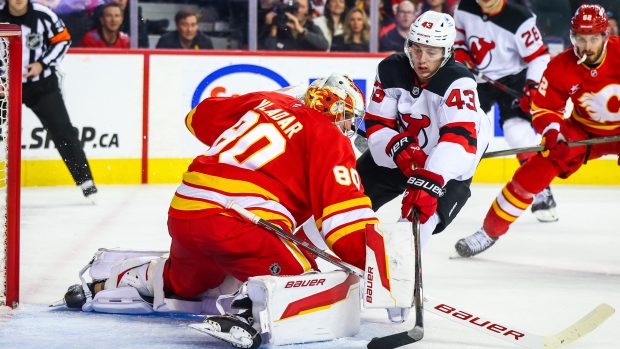 Brankář Calgary Flames Daniel Vladař zasahuje proti Lukeu Hughesovi z New Jersey Devils