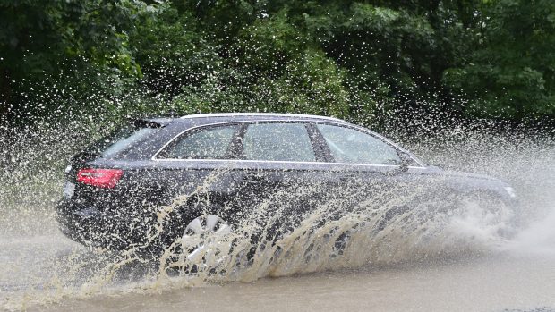 Automobil projíždí zaplavenou silnicí poblíž Černošic.