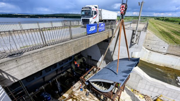 Dělníci usazují jeřábem druhou polovinou klapkového uzávěru bezpečnostního přelivu Nechranické přehrady,