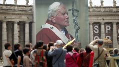 Poutníci stojí před billboardem Jana Pavla II. ve Vatikánu.