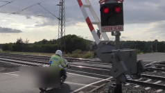 Policista podjíždí padající závory na železničním přejezdu.