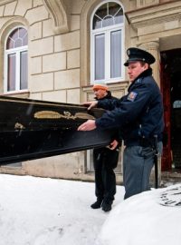 Pohřební služba vynáší tělo hudebníka v rakvi z domu, kde byl spolu s manželkou zavražděn.