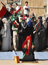 Žena se modlí, zatímco jiní oslavují konec Kaddáfího na náměstí v Tripolisu