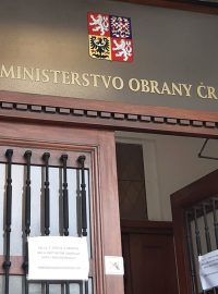 „Od 15. července 2020 je v objektu MO-A (ministerstva obrany-A) opět nutné zakrývat ústa i nos rouškou!!!“ stojí na bílém papíru přilepeném na dveřích a dole je ještě poznámka: „!Nařízeno hlavní hygieničkou AČR!“