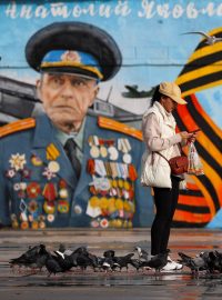 Lidé krmí ptáky před nástěnnou malbou zobrazující veterána z druhé světové války a člena vojensko-vlasteneckého hnutí Ruské armády mládeže, na nábřeží v Jaltě. (Ilustrační foto)
