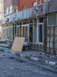 Muž uklízí rozbité sklo vedle budovy zasažené ostřelováním, které místní úřady označily za útok ukrajinské armády v ruském Belgorodu 9. května 2024